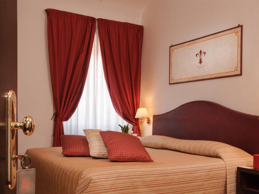 Camera d'albergo con letto matrimoniale, tende rosse e arredo elegante.