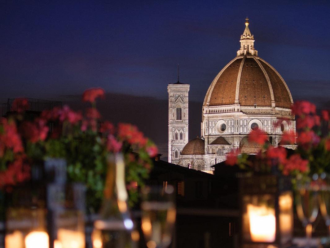 Night view of Florence Cathedral with candles and flowers in the foreground.