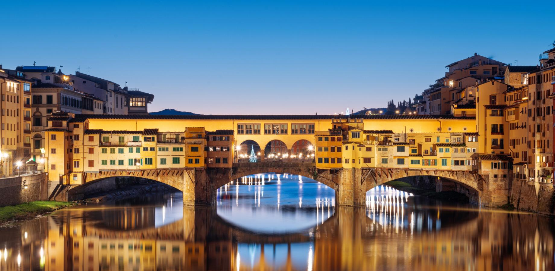 Ponte Vecchio à Florence illuminé la nuit, reflété dans le fleuve Arno.