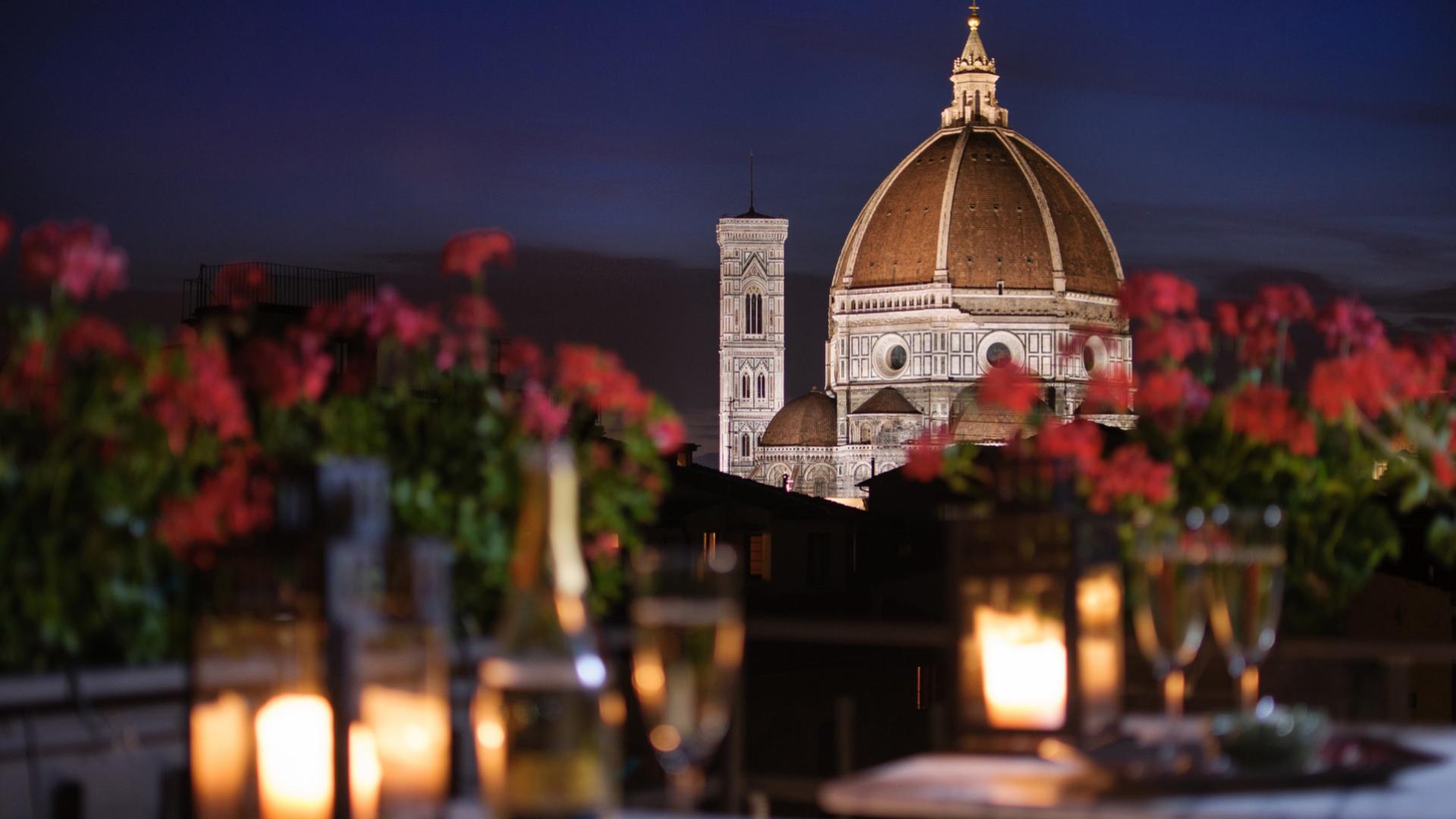 Vista notturna del Duomo di Firenze con candele e fiori in primo piano.