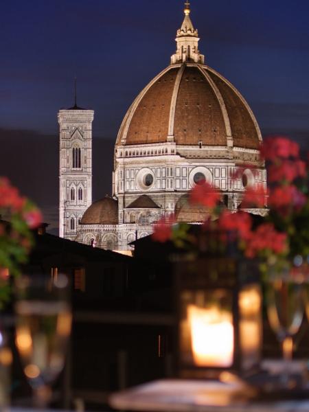 Vista notturna del Duomo di Firenze con fiori e candele in primo piano.