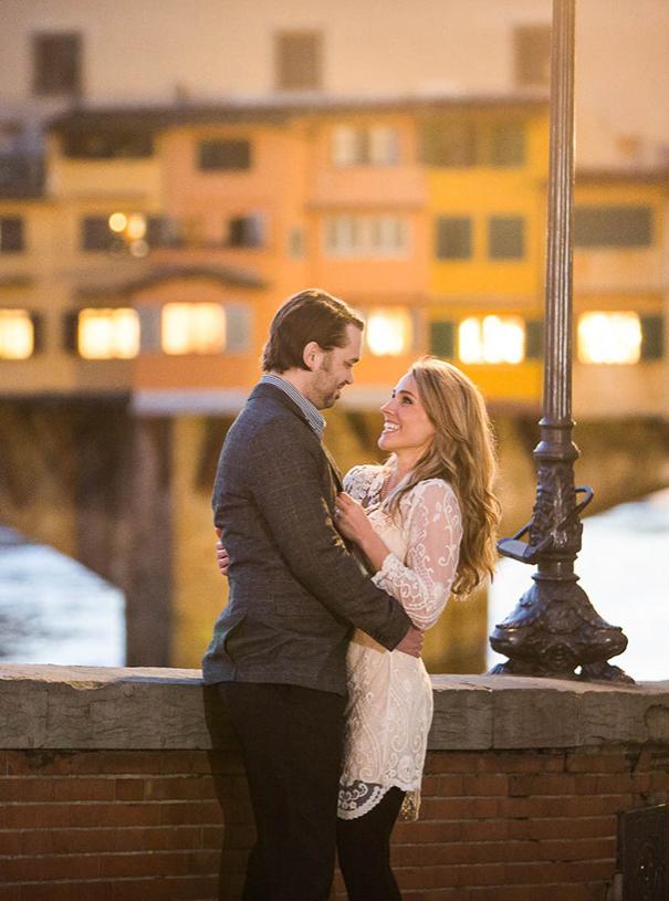 Happy couple embracing in front of a lit bridge.